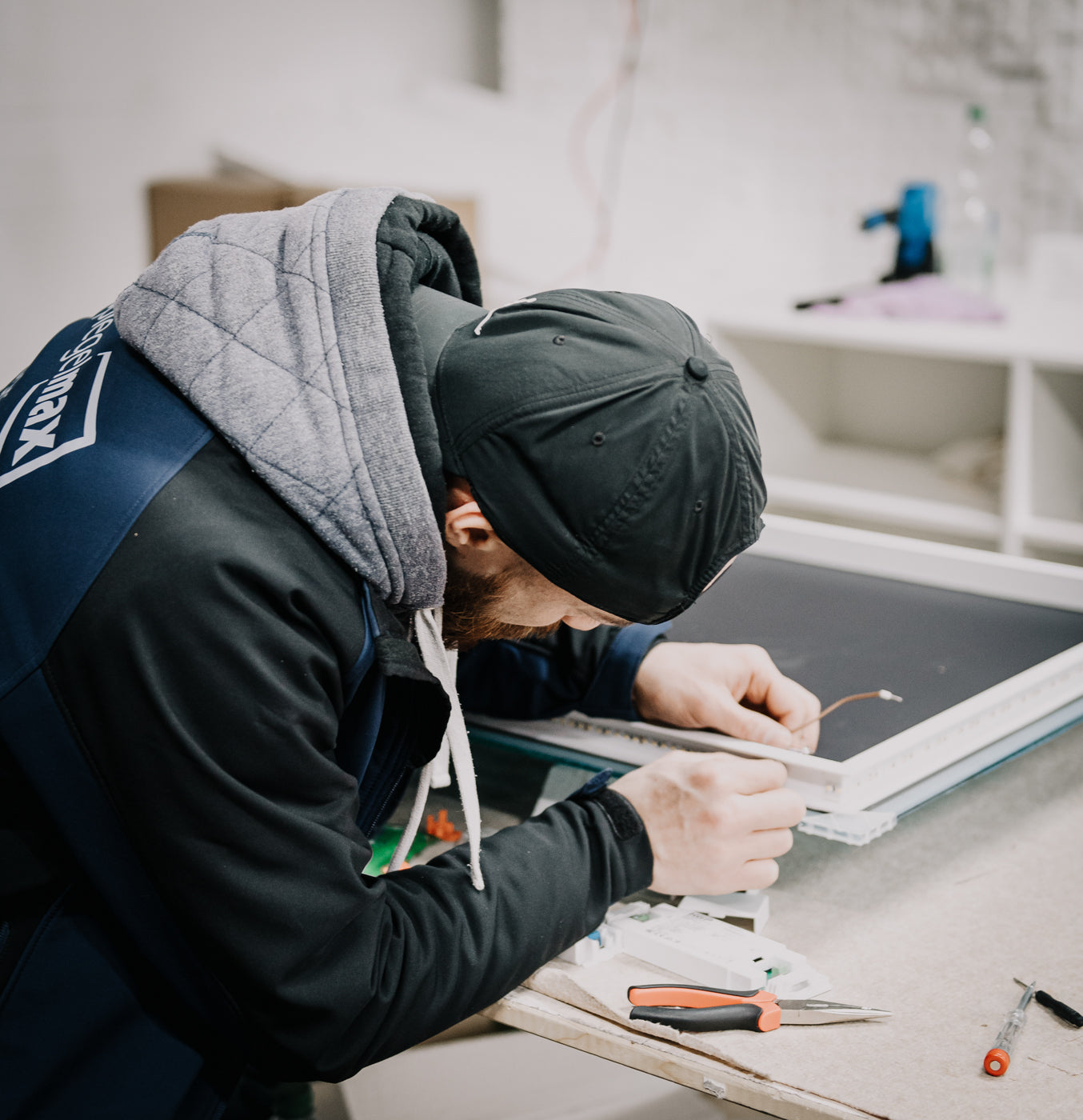 Mitarbeiter verkabelt LED-Lichtleiste in einem Spiegelrahmen an der Werkbank – elektrische Endmontage