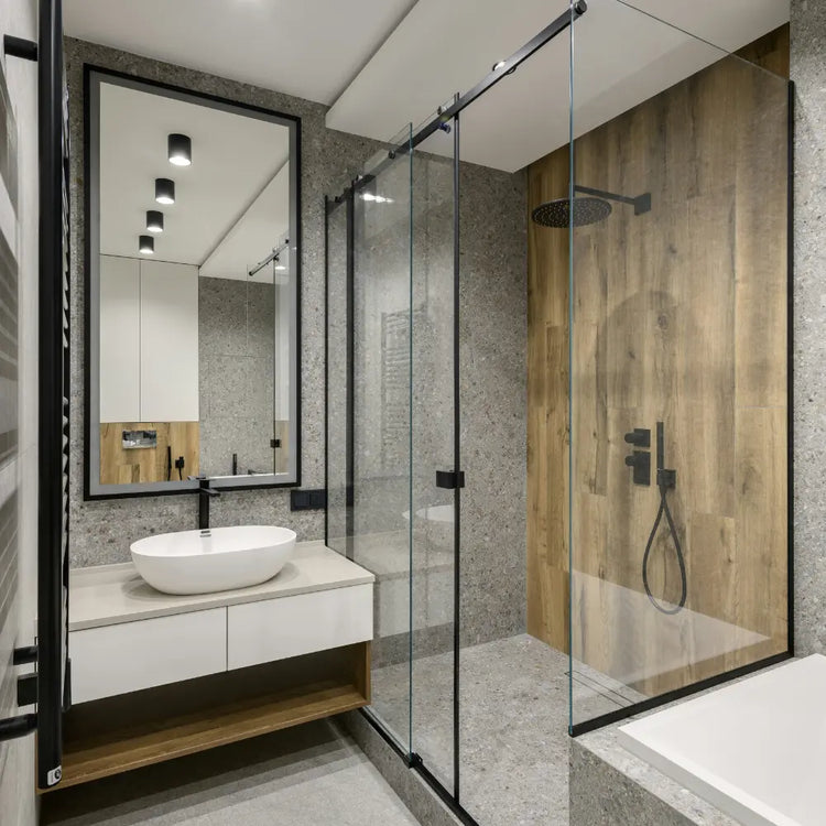 Modernes Badezimmer mit Glas-Duschwand, Waschbecken auf Holzplatte, großem Wandspiegel und grauer Steinverkleidung.