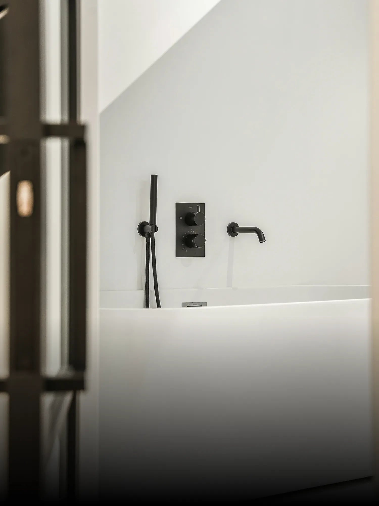 Badewanne mit schwarzer Armatur und Handbrause vor weißer Wand, ausgestattet mit schlichten Badmöbel Accessoires.