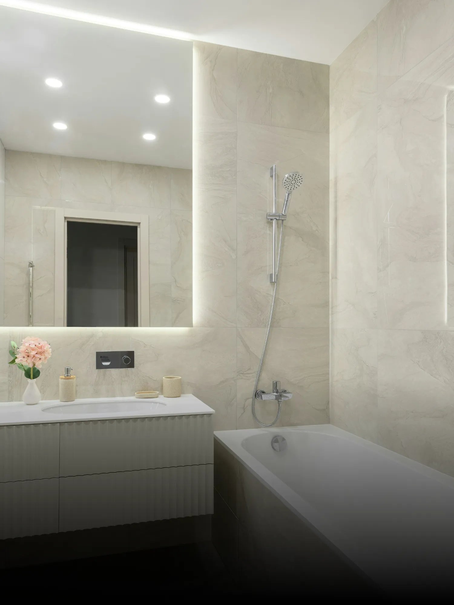 Beleuchteter Badspiegel über einem Waschbecken mit cremefarbenen Fliesen und Badewanne mit Handbrause.