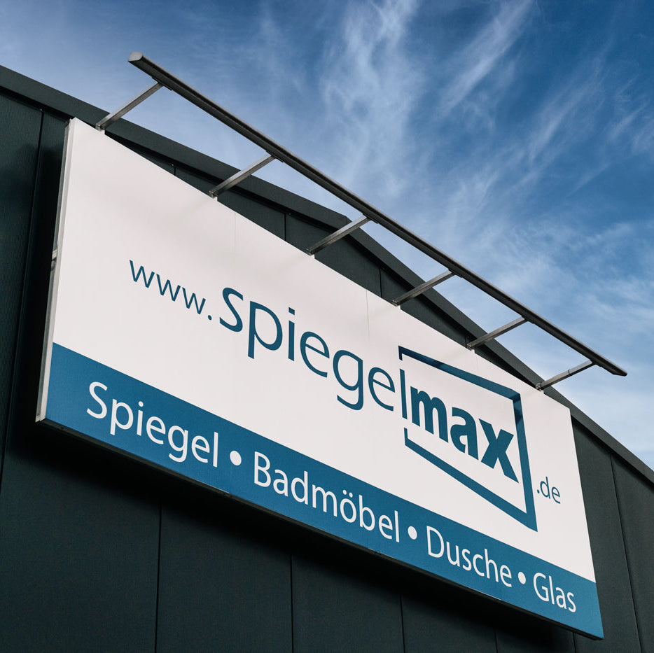 Firmenschild von Spiegelmax an einem Gebäude mit dem Schriftzug Spiegel, Badmöbel, Dusche und Glas vor blauem Himmel