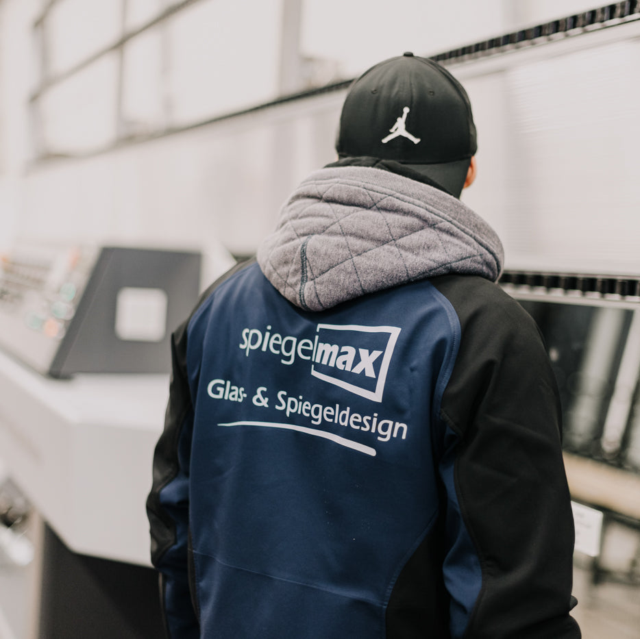 Mitarbeiter in Spiegelmax Arbeitskleidung steht in der Produktionshalle vor Maschinen zur Glas- und Spiegelbearbeitung