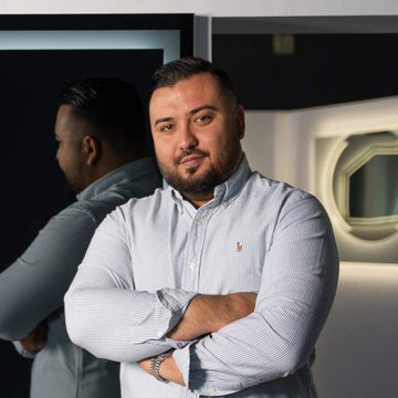 Person steht mit verschränkten Armen vor einem beleuchteten Spiegel im Spiegelmax Showroom