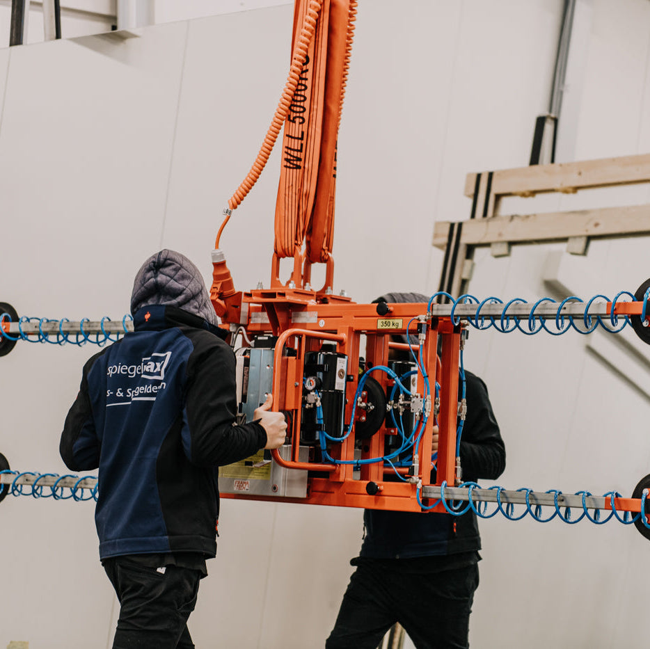 Mitarbeiter von Spiegelmax bedienen in der Produktionshalle einen großen Vakuumheber zum Transport schwerer Glasplatten